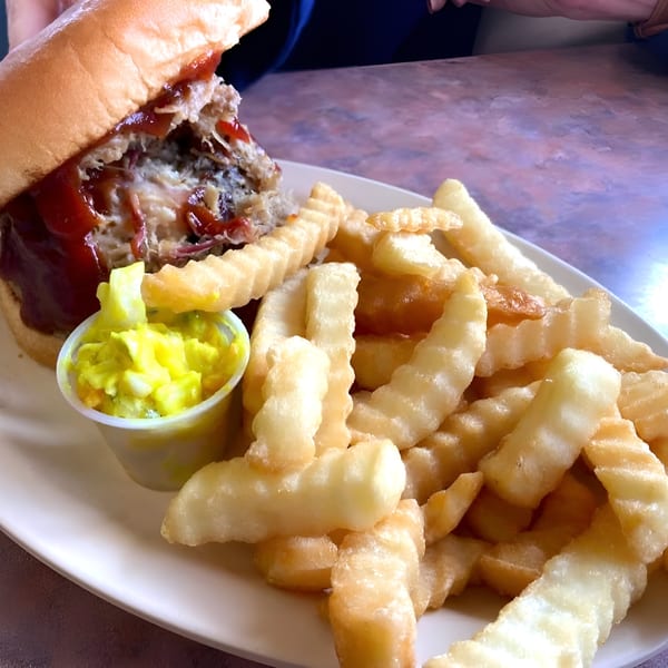 Chuck's BBQ pulled pork sandwich with barbecue sauce, crinkle-cut fries, and coleslaw on a white plate.
