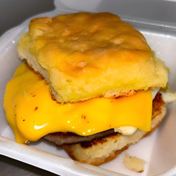 A Chuck's BBQ breakfast biscuit with sausage, egg, and melted cheese in a white takeout container.