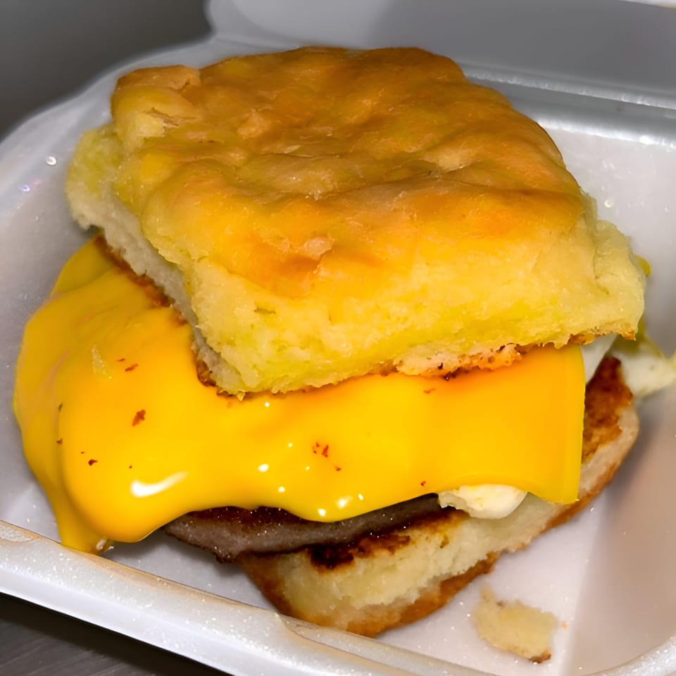 A Chuck's BBQ breakfast biscuit with sausage, egg, and melted cheese in a white takeout container.